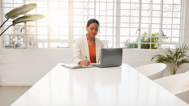 Woman sitting at a conference table with a laptop and notebook.