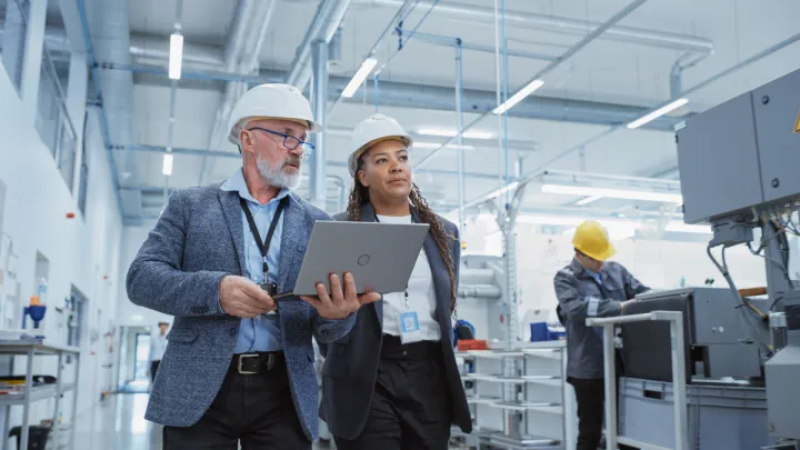 Two individuals wearing hard hats walking through a plant
